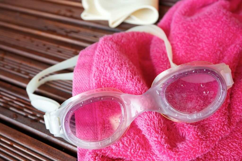 Swim goggles, towel, and a swim cap are displayed
